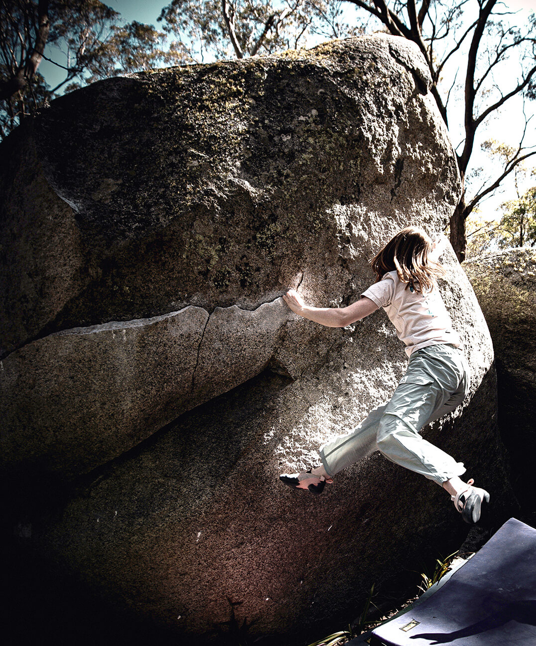 Climber on a sunlit outdoor boulder with crash pad below